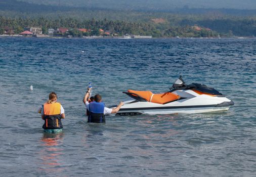 Tourists enjoy driving jet ski on the ocean. A young couple boardes a jetbike.
