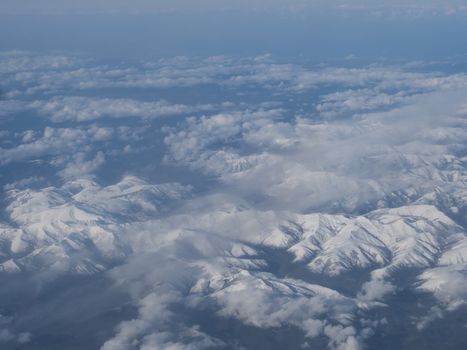 Aerial view of snow covered french and spanish pyrenees with snow covered mountains viewed from an airplane. Blue sky white clouds background.