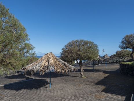 Parasol umbrellas from dry palm tree leaves on La Fajana promenade with sea and blue sky background at La Palma, Canary Islands, Spain.