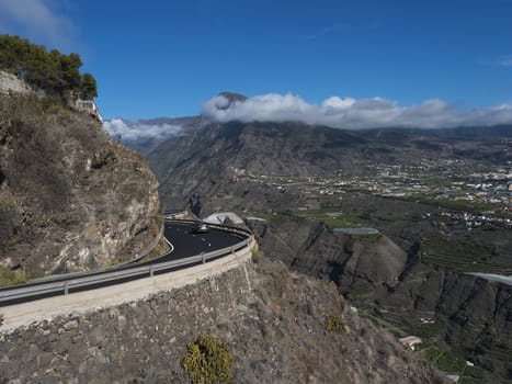 View on car at curved winding asphalt road in steep rocky mountain slope with subtropical volcanic landscape of La Palma, Canary Islands, Spain.