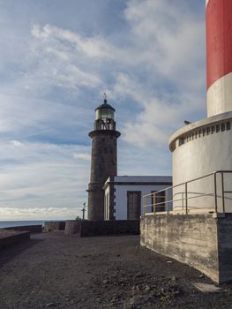 View of two lighthouses, old stone and white-red striped with volcanic rock field at Fuencaliente, La Palma, Canary Islands. Blue sky white clouds background.