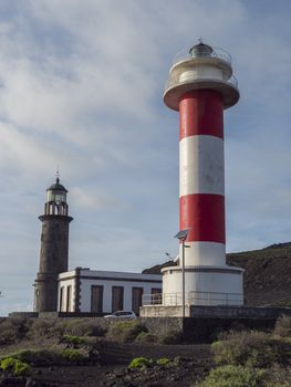 View of two lighthouses, old stone and white-red striped with volcanic rock field at Fuencaliente, La Palma, Canary Islands. Blue sky white clouds background.