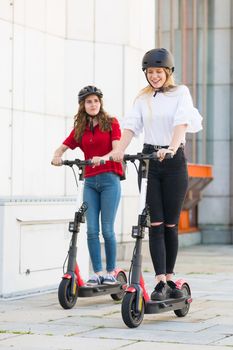 Trendy fashinable teenager girls riding public rental electric scooters in urban city environment. New eco-friendly modern public city transport in Ljubljana, Slovenia.