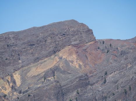 View on colorful vocanic rock of crater Caldera de Taburiente with mountain peak Roque de los Muchachos on the island La Palma, Canary Islands, Spain. Blue sky background.