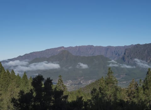Volcanic landscape with lush green pine trees, colorful volcanoes and lava rock field along path Ruta de los Volcanes, hiking trail at La Palma island, Canary Islands, Spain, Blue sky background.