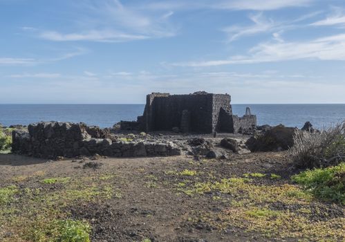Old lava stone and wooden rustic door, blue house, white apartments, palm trees, green hills and blue sky at Canary islands village