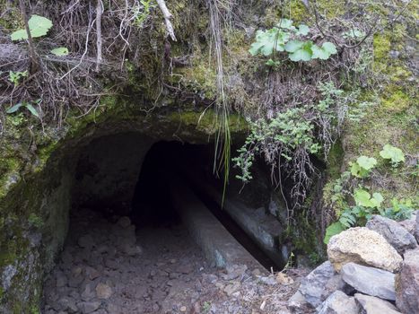 Dark entrance to the tunnel of water duct levada at hiking trail Casa del Monte to Los Tilos at mysterious laurel forest. Beautiful nature reserve on La Palma, Canary islands, Spain.