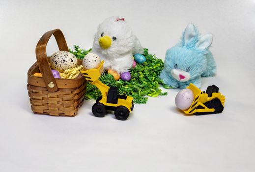 Easter themed photo of stufed bunny and hen with decorated Easter eggs, a basket,  and a child's toy construction vehicles.