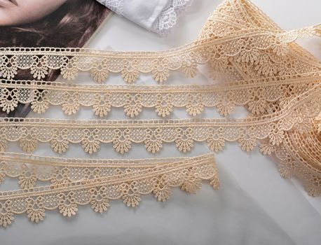 Tapes of beige gentle guipure, beauty lace fabric on light background. Elastic material. Using for Atelier and needlework store.