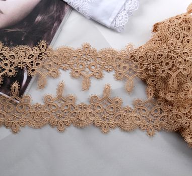 Tapes of beige gentle guipure, beauty lace fabric on light background. Elastic material. Using for Atelier and needlework store.