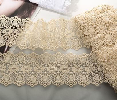 Tapes of beige gentle guipure, beauty lace fabric on light background. Elastic material. Using for Atelier and needlework store.