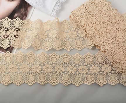 Tapes of beige gentle guipure, beauty lace fabric on light background. Elastic material. Using for Atelier and needlework store.