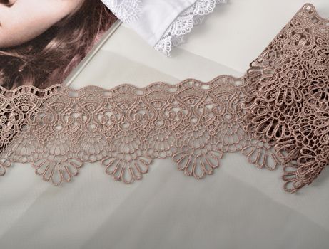 Tapes of beige gentle guipure, beauty lace fabric on light background. Elastic material. Using for Atelier and needlework store.