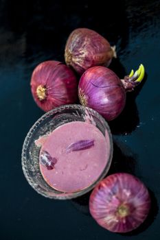 Close up of glass bowl full of extracted onion pulp in it and raw onions or pyaaj or Allium cepa.