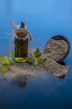 Ayurvedic herb brahmi or Waterhyssop oil in a small transparent glass bottle along with its powder on wooden surface.