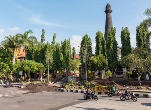 Bali, Indonesia -- February 28, 2016. Motorcyclists ride down a city street near the ancient Courts of Justice on a hot sunny day in Bali, Indonesia.