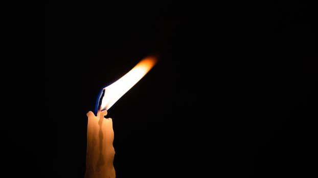 Close-up of a yellow candle shining in a black background.