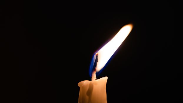 Close-up of a yellow candle shining in a black background.