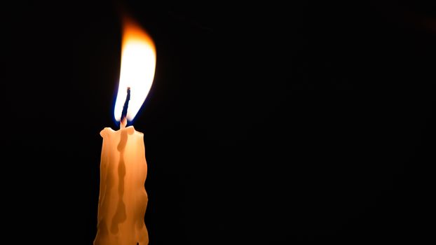 Close-up of a yellow candle shining in a black background.