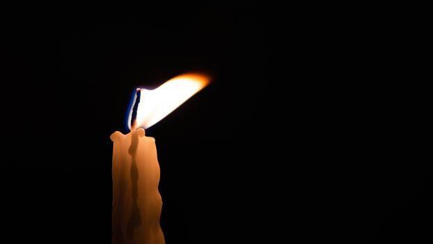 Close-up of a yellow candle shining in a black background.