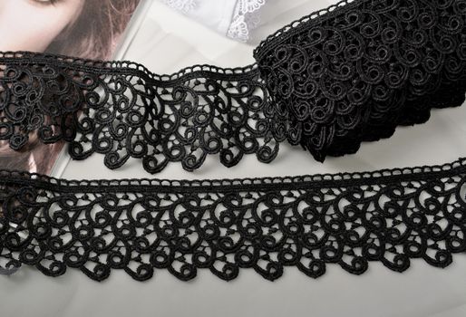 Tapes of black gentle guipure, beauty lace fabric on light background. Elastic material. Using for Atelier and needlework store.
