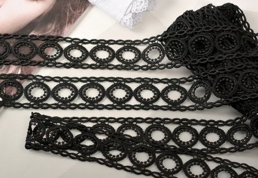 Tapes of black gentle guipure, beauty lace fabric on light background. Elastic material. Using for Atelier and needlework store.