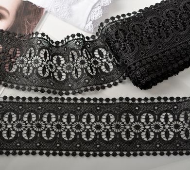 Tapes of black gentle guipure, beauty lace fabric on light background. Elastic material. Using for Atelier and needlework store.