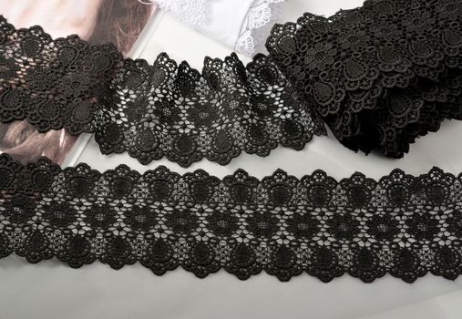 Tapes of black gentle guipure, beauty lace fabric on light background. Elastic material. Using for Atelier and needlework store.