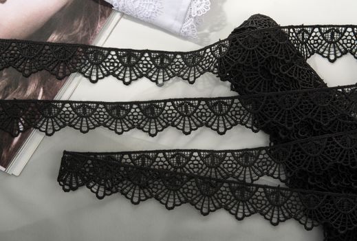 Tapes of black gentle guipure, beauty lace fabric on light background. Elastic material. Using for Atelier and needlework store.