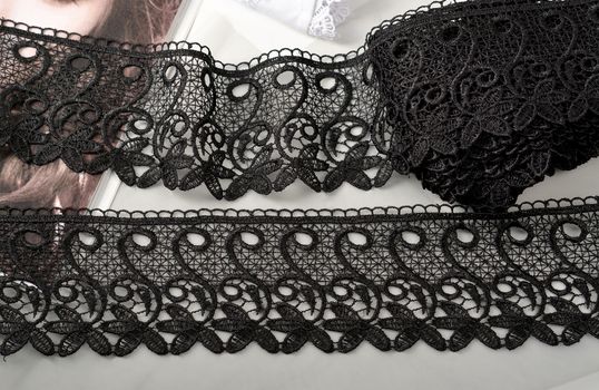 Tapes of black gentle guipure, beauty lace fabric on light background. Elastic material. Using for Atelier and needlework store.