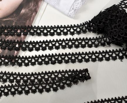 Tapes of black gentle guipure, beauty lace fabric on light background. Elastic material. Using for Atelier and needlework store.