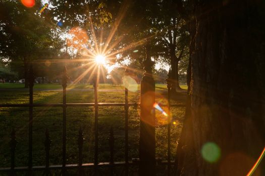 Long shadows through wrought iron fence surrounding La Fayette Park with lens flare aged photo effect and haze at sunset  St Louis Missouri USA