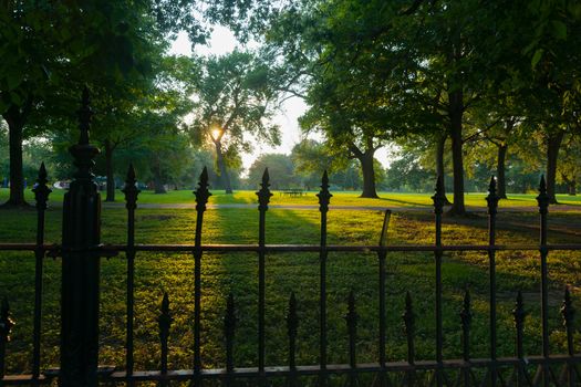 Long shadows through wrought iron fence surrounding La Fayette Park with lens flare aged photo effect at sunset  St Louis Missouri USA