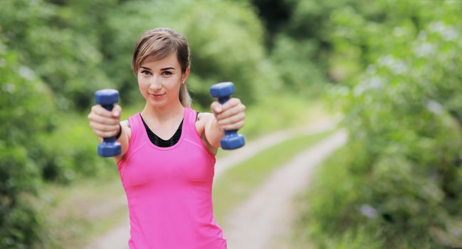 The girl is engaged in sports with weights in nature forest. Motivation healthy fit living. Running shoe of the person running in nature with beautiful sunlight. Woman warming up before running