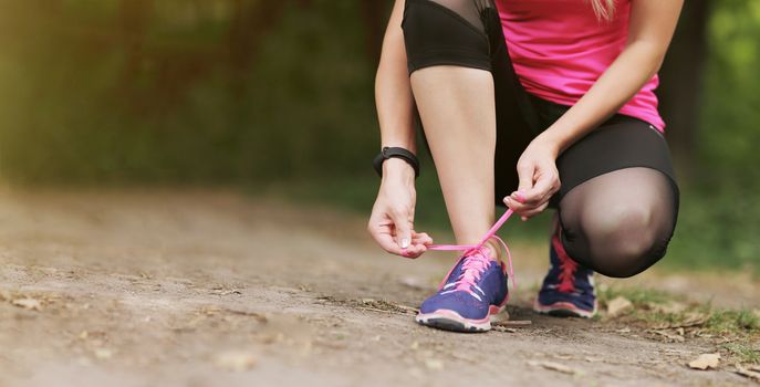 Young fitness woman tying shoelace running sneakers. In the morning forest trail. Motivation healthy fit living. Running shoe of the person running in nature with beautiful sunlight.