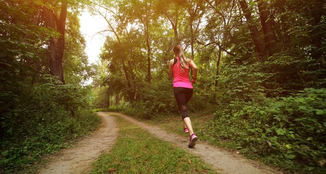 Young fitness woman running in the morning forest trail. Motivation healthy fit living. Running shoe of the person running in nature with beautiful sunlight. Woman warming up before running