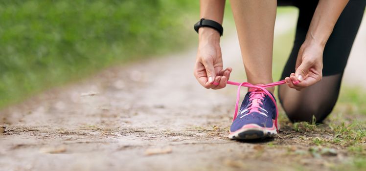 Young fitness woman tying shoelace running sneakers. In the morning forest trail. Motivation healthy fit living. Running shoe of the person running in nature with beautiful sunlight.