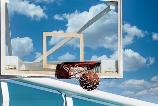 A basketball dropping into the net of a goal against a blue sky