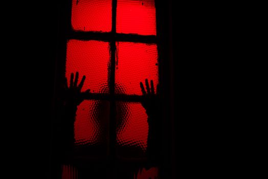 Scary sihouette of person leaning against window in dark