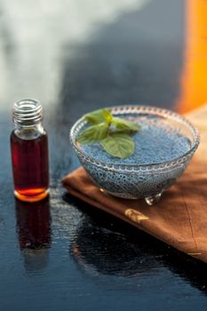Glass bowl full of soaked sabja seeds or falooda seeds or sweet basil seeds with its extracted essence or essential oil in a transparent glass bottle on wooden surface.