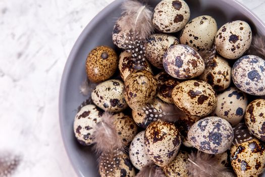 pile of Easter quail eggs on gray fabric cotton rag on concrete background, Round ceramic plate. Space for text