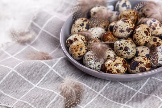 pile of Easter quail eggs on gray fabric cotton rag on concrete background, Round ceramic plate. Space for text