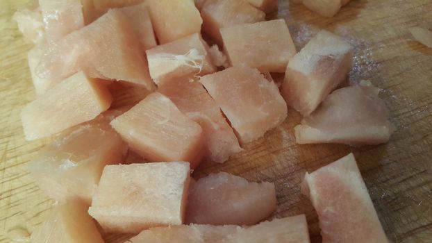 Close up top view of fresh finely chopped chicken meat cubes. White meat small steaks with meat fat.