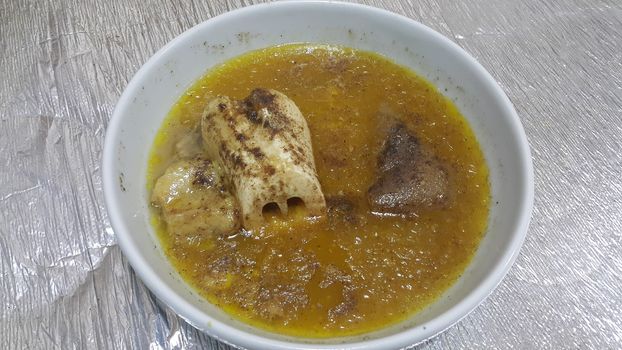Top view of siri paaye or paya dish garnished with diced ginger, long coriander leaves and fresh sliced lemon. This dish is popular in Pakistan and Bangladesh