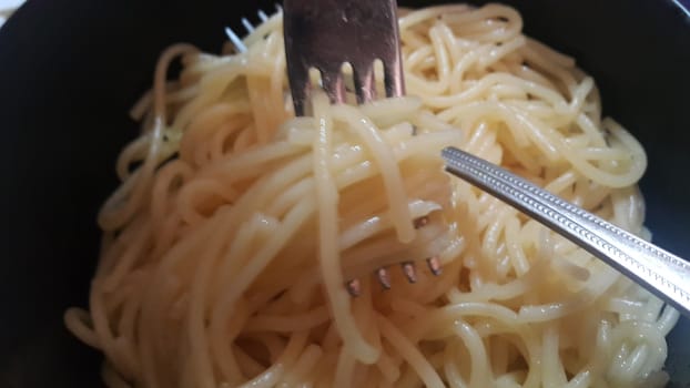 close up view of swirling noodles or spaghetti pasta in a bowl with silver fork