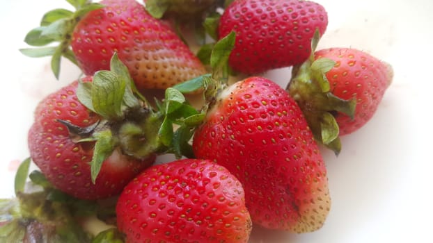 Top view with selective focus of sweet fresh strawberries with green leaves in plate on rustic white background.