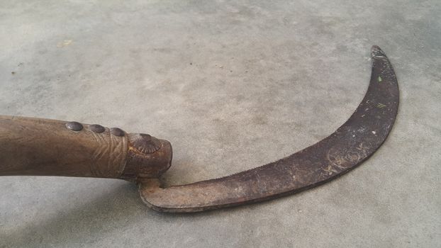 Close-up view of an old sickle (bagging hook or reaping-hook) on the concrete surface. Traditional hand-held agricultural tool.