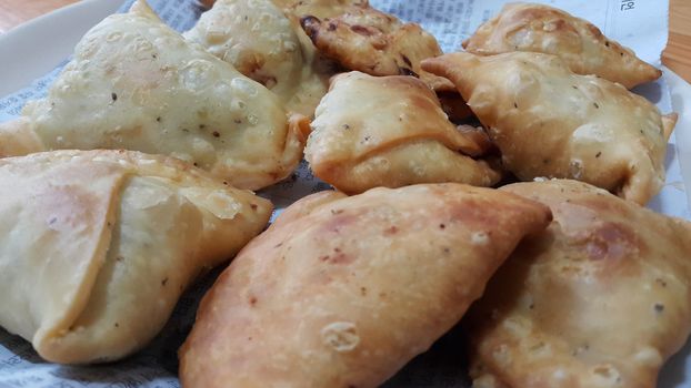Closeup of delicious home made spicy and crunchy samosa pastries placed in a white ceramic plate on wooden floor