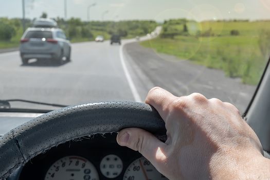 the driver hand on the steering wheel of a car that is passing on a country highway