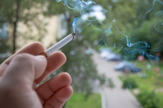 View of the hand of a Smoking man with a Smoking cigarette from the window of the apartment into the yard and the street